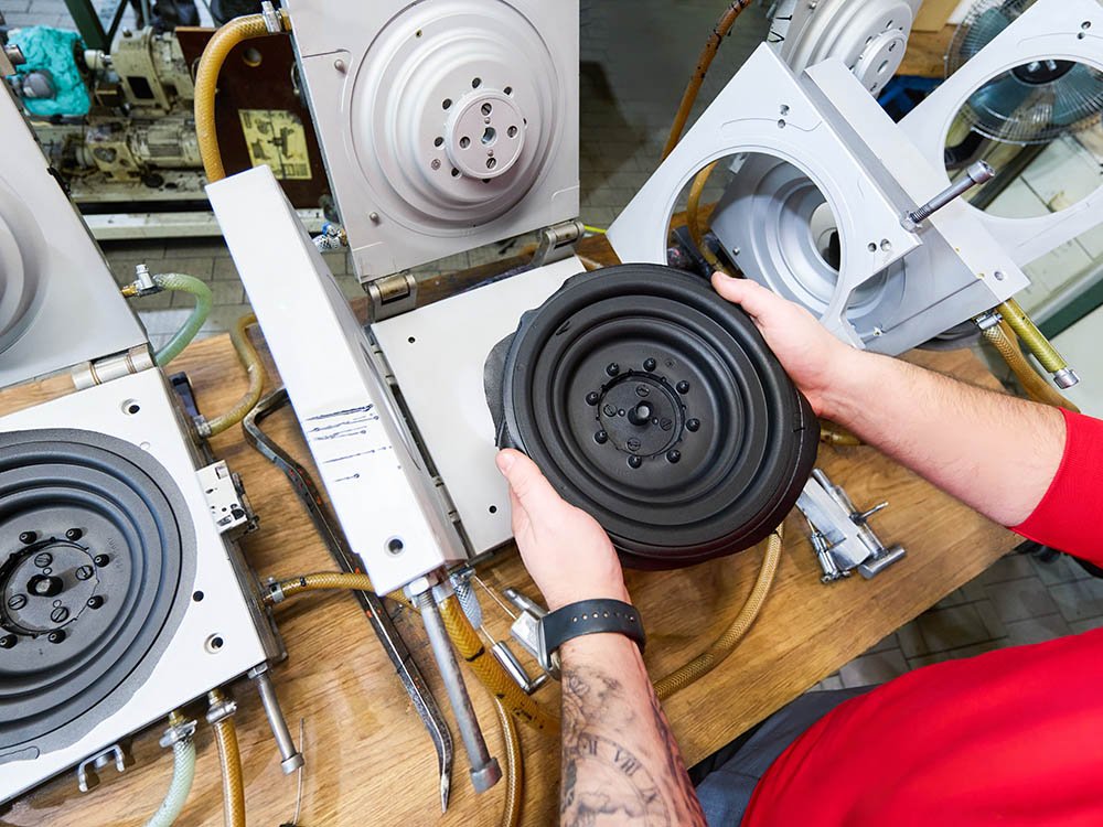 Elastomer-Schaum Formteil nach der Fertigung in der Produktion Mitarbeiter hält ein rundes Elastomer-Schaum Bauteil vor einer Produktionsanlage